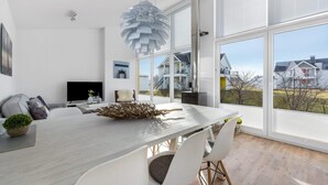 A modern dining area with a large table, white chairs, and a unique chandelier.