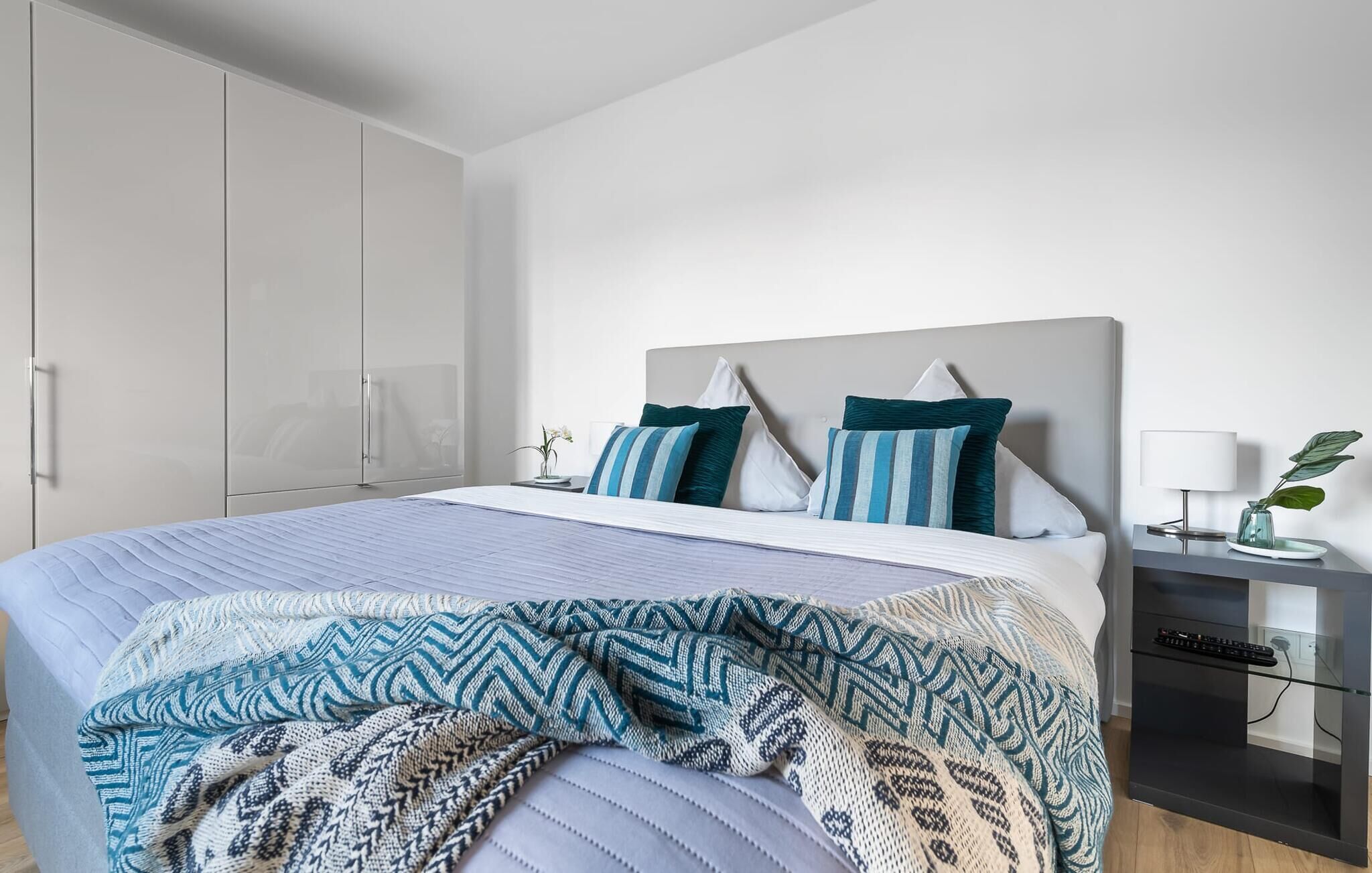 A modern bedroom with a large bed, a nightstand, a desk, and a wardrobe.