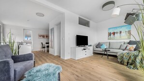 A modern living room with a grey sofa, a fluffy ottoman, a TV on a white cabinet, and a painting on the wall. - Lovely apartment in Olpenitz with sauna (Olpenitz)
