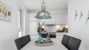 A modern dining area with a white table, black chairs, a decorative centerpiece, and a kitchen in the background. - Lovely apartment in Olpenitz with sauna (Olpenitz)