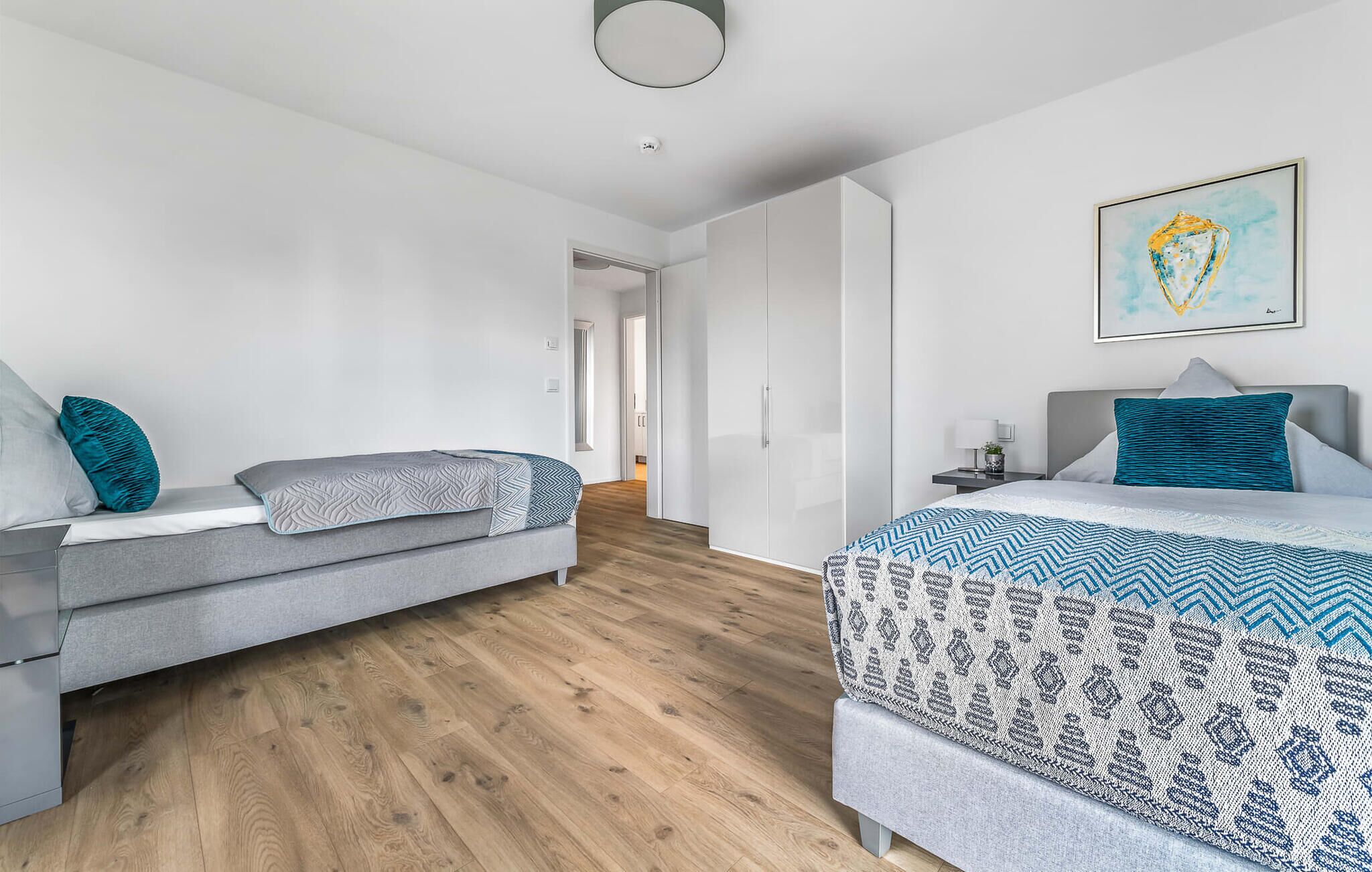 Ein modernes Schlafzimmer mit grauem Sofa, einer gemusterten Bettdecke und einem Bild an der Wand.