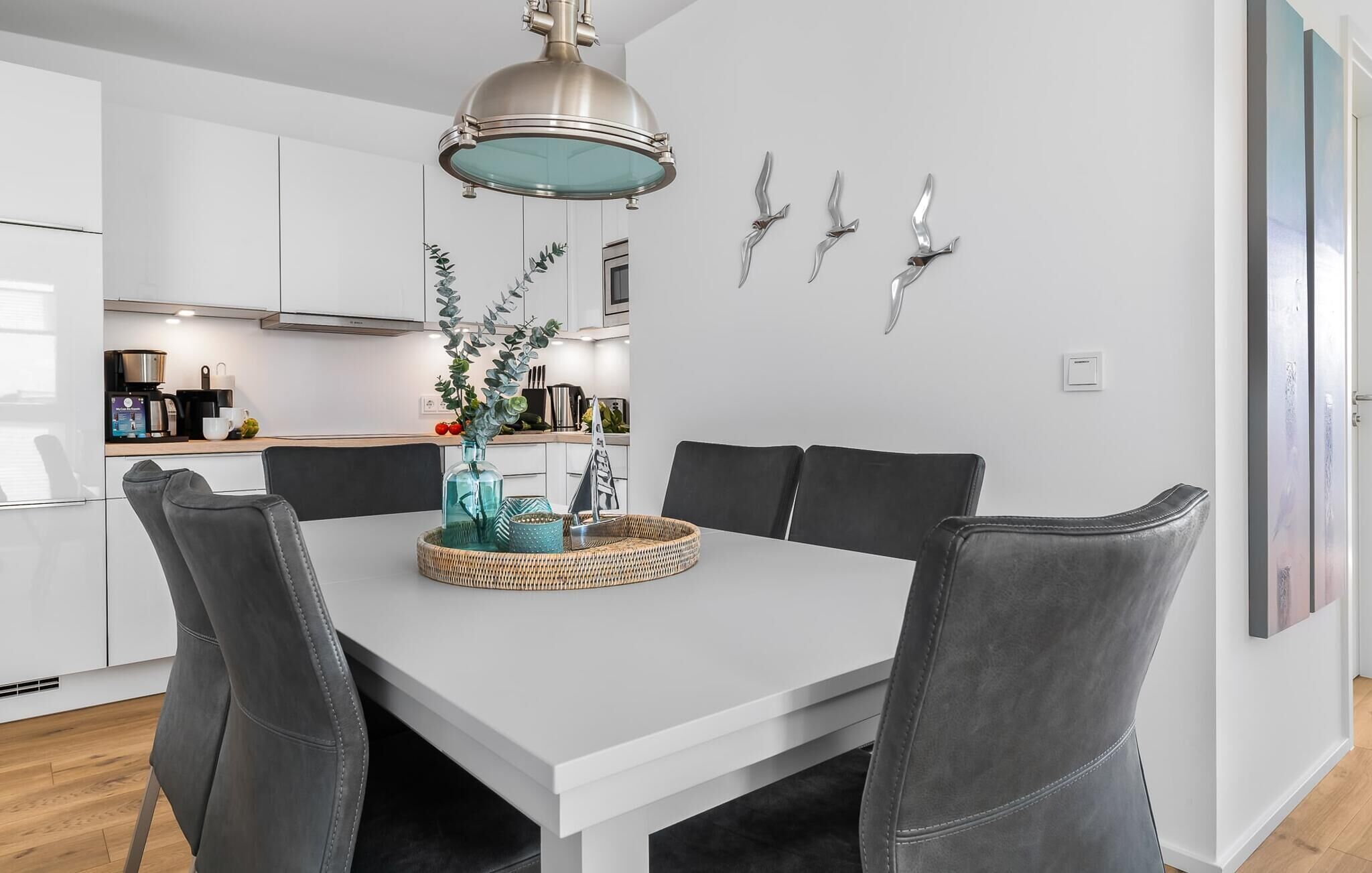 A modern dining area with a white table, grey upholstered chairs, and a decorative centerpiece.