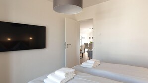 A hotel room with two beds, a TV mounted on the wall, and a door leading to a dining area.