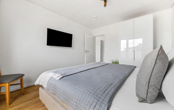 Ein modernes Schlafzimmer mit Bett, Sessel, Fernseher und Fenster.