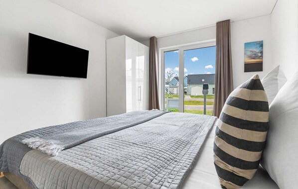 Un dormitorio con cama, televisión, ventana con cortinas y vistas al exterior.