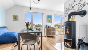 Un salon moderne comprenant un coin repas, un poêle à bois noir et de grandes fenêtres donnant sur l’extérieur.
