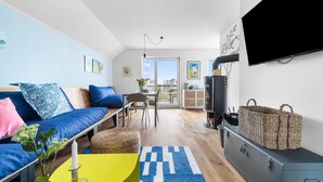 Un salon moderne avec un canapé, une table basse et un téléviseur. On y trouve également un panier en osier et un meuble gris.
