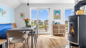 Un salon moderne comprenant un coin repas, un poêle à bois noir et un balcon offrant une vue sur le quartier.