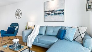 A modern living room with a light blue sectional sofa, a blue armchair, a decorative compass wall art, a framed abstract painting, and a small table with a lamp and decorative items. - Pet friendly apartment in Olpenitz (Olpenitz)