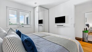 A modern bedroom with a large bed, two TVs mounted on the wall, and a window providing a view of the outdoors. - Pet friendly apartment in Olpenitz (Olpenitz)