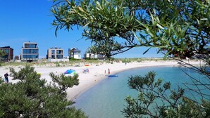 Une plage bordée de bâtiments modernes, avec un ciel dégagé et une mer calme.