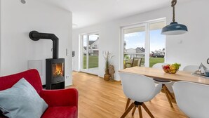 A modern living room with a wood-burning stove, a red sofa, a dining area with white chairs, and a view of the outside.