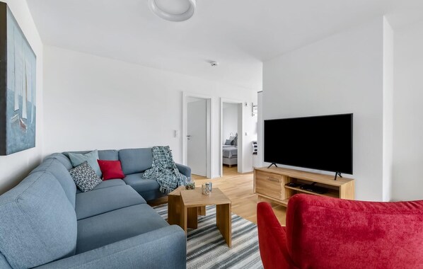 A modern living room with a grey sofa, a red chair, a wooden coffee table, and a large flat-screen TV on a wooden stand. - Beautiful apartment in Olpenitz (Olpenitz)