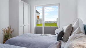 A bedroom with a large bed, a wardrobe, and a view of a building and grassy area through a glass door.