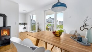 A modern kitchen with a wood-burning stove, a washing machine, and a dining area with a wooden table and white chairs.