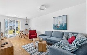 Un salon moderne avec un canapé gris, un fauteuil rouge et un tableau représentant des voiliers.