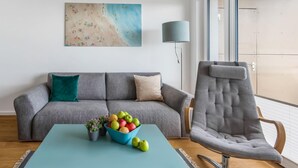 A living room with a grey sofa, a blue coffee table with a bowl of fruit, and a grey armchair. - Beautiful apartment in Olpenitz (Olpenitz)