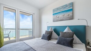 A bedroom with a large bed, a view of the sea through the window, and a painting of birds on the wall. - Beautiful apartment in Olpenitz (Olpenitz)