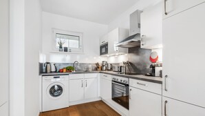A modern kitchen with white cabinetry, a built-in washing machine, a stove, and a microwave. - Beautiful apartment in Olpenitz (Olpenitz)