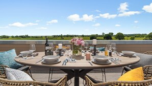 A round dining table set for four with plates, cutlery, glasses, and a bottle of wine, overlooking a scenic landscape. - Beach front apartment in Olpenitz (Olpenitz)