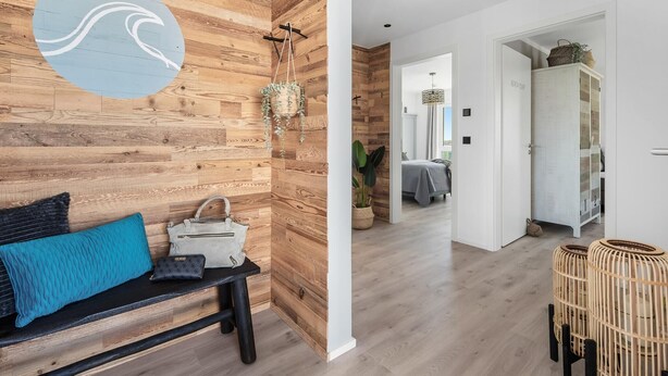 A modern interior with a wooden wall, a bench with cushions, a hanging plant, and a wicker basket. - Beach front apartment in Olpenitz (Olpenitz)