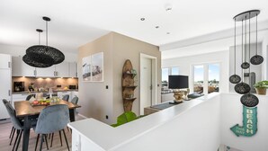 A modern kitchen with white cabinets, a dining area with a wooden table and chairs, and a view of the living area with a large window. - Beach front apartment in Olpenitz (Olpenitz)