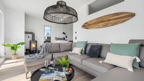 A modern living room with a grey sofa, a black coffee table with magazines and glasses, a potted plant, and a large wooden board on the wall. - Beach front apartment in Olpenitz (Olpenitz)