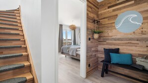 A modern interior with a wooden staircase, a bed in the adjacent room, and a bench with cushions. - Beach front apartment in Olpenitz (Olpenitz)