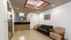 A reception area with a reception desk, a black leather sofa, a beige armchair, and a small table. - Aryaas Residency Nettoor (Kanayannur)