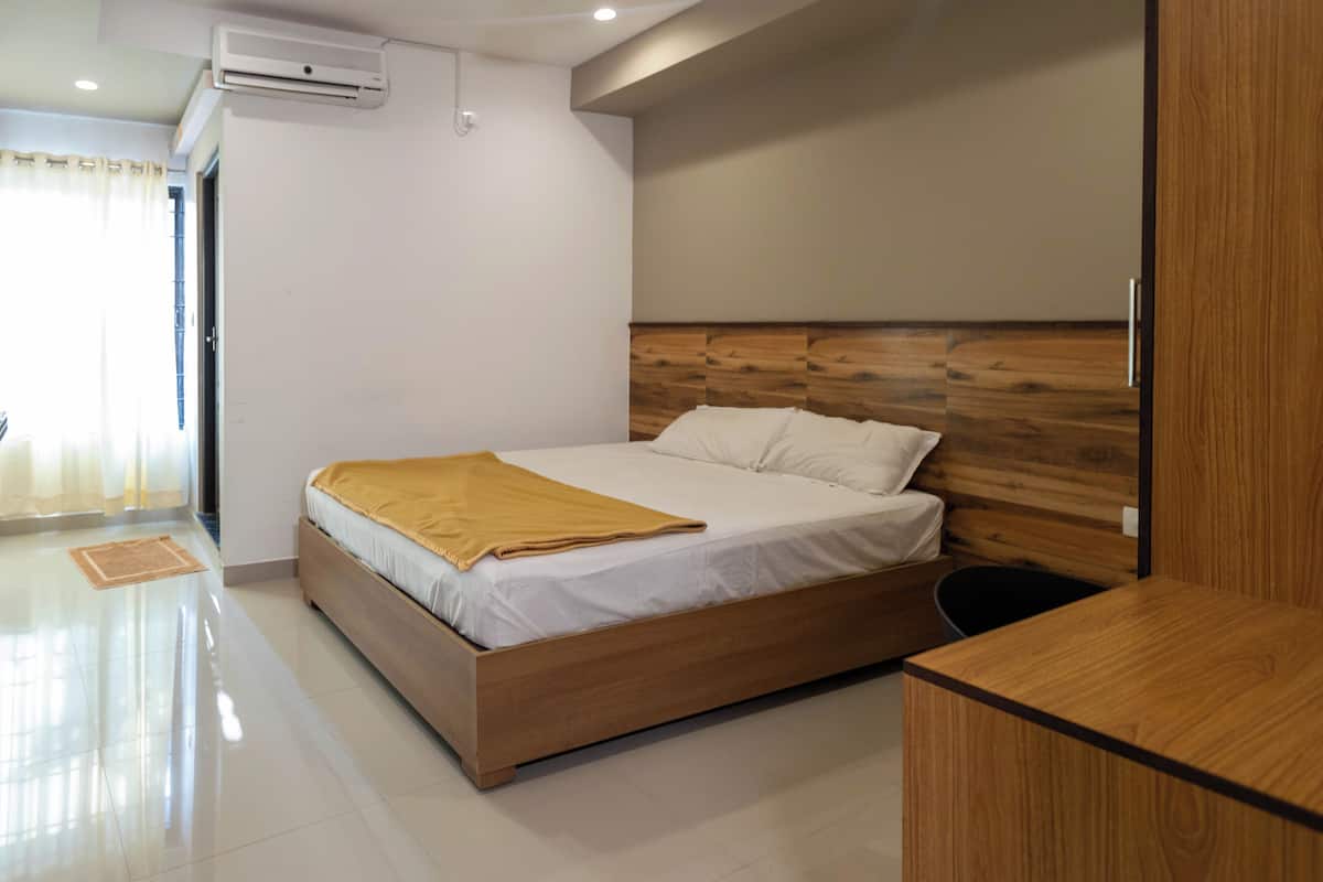 A modern bedroom with a wooden headboard, a bed with white linens, a wooden bedside table, and a small desk.
