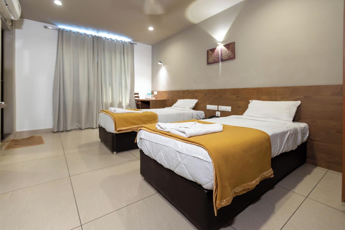 A hotel room with two beds, a wooden headboard, a small bedside table, and a curtain.