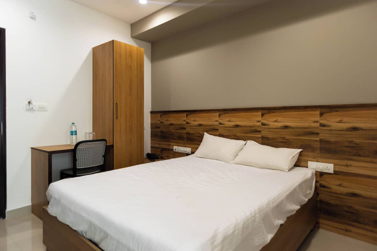 A bedroom with a wooden headboard, a bed with white bedding, a desk with a chair, and a wardrobe.