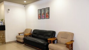 A living room with a black leather sofa, two beige armchairs, and a small wooden coffee table. There are three framed pictures on the wall. - Aryaas Residency Nettoor (Kanayannur)