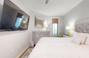 A bedroom with a large bed, a dresser, a television mounted on the wall, a window with a view, and a decorative headboard. - Beautiful 1-bedroom condo with WiFi, at Sandestin Resort - Elation Building (Miramar Beach)