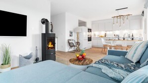 En moderne stue med pejs, sofa og spiseområde med et køkken i baggrunden.