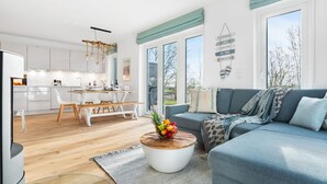 En moderne stue med en blå sofa, et træbord med frugt og udsigt til det fri gennem store vinduer.