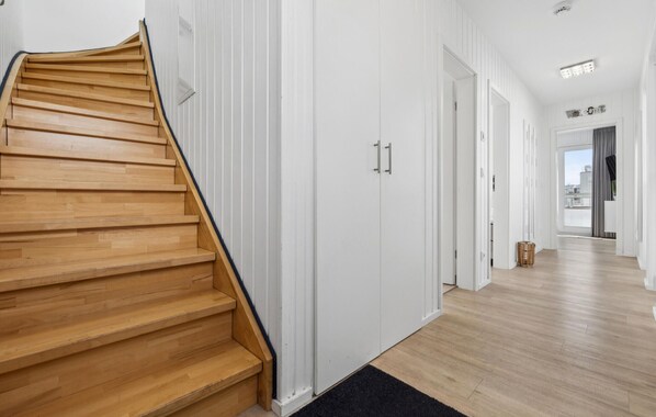 Um interior moderno com escada de madeira que leva a um corredor com portas brancas e vista para a cidade.