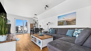 Un salon moderne avec un canapé gris, une table basse en bois et un tableau représentant un paysage côtier.