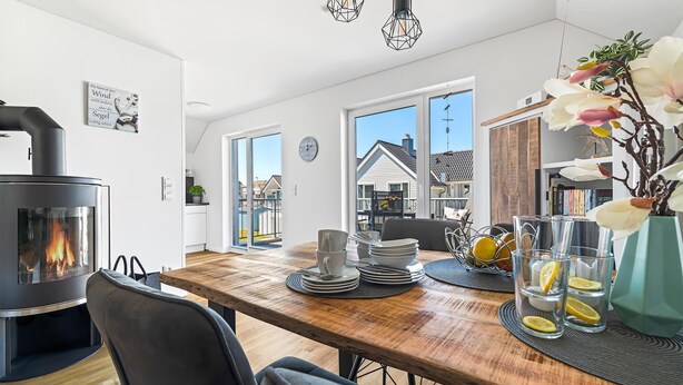Une cuisine moderne dotée d’un poêle à bois encastré, un coin repas avec une table en bois et une vue sur le quartier grâce à de grandes fenêtres.