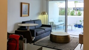 Un salon moderne comprenant un canapé, une table basse ronde, une table à manger et un balcon aménagé avec du mobilier d’extérieur.