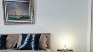 Une chambre à coucher avec un lit, des oreillers, une table de chevet avec une lampe et un tableau encadré accroché au mur.