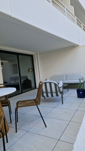 An outdoor patio area with a white sofa, wicker chairs, and a small potted plant. - Archipelago terrace side (Valras-Plage)