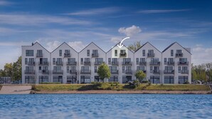 Un immeuble moderne à plusieurs étages, doté de balcons, situé près d’une étendue d’eau.