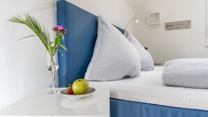 Une chambre à coucher moderne avec un lit, des oreillers, une table de chevet agrémentée d’une plante et de fruits, et un luminaire fixé au mur.