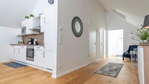 Une cuisine moderne avec des meubles blancs, un four encastré et un four à micro-ondes. On y trouve également un coin repas avec un canapé foncé et une table basse.