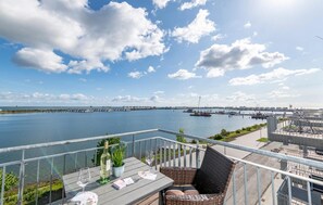 A balcony with a view of a marina, a dining table with a bottle and glass, and a wicker chair. - Stunning apartment in Olpenitz (Olpenitz)