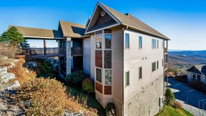 A modern two-story house with a balcony, stone foundation, and a view of the surrounding landscape. - Comfy Condo At Top Of Sugar Mtn - Ski In Ski Out - AC, WiFi (Sugar Mountain)