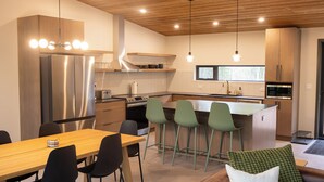 A modern kitchen with a central island, bar stools, and a dining area with a wooden table and chairs. - Spruce House: The Perfect Summer Retreat with Hiking, Swimming, and More (Copper Harbor)