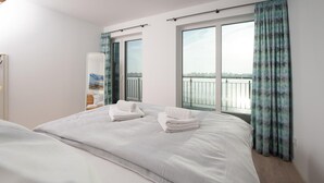 Ett hotellrum med en stor säng, två vita handdukar, en glasdörr som leder ut till en balkong och utsikt över en sjö eller ett annat vattendrag.