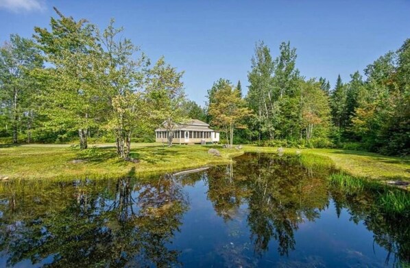 Een huis, omringd door een vijver en bomen.